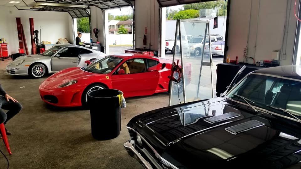 Garage with a red Ferrari, silver Porsche, and black car. Work in progress.