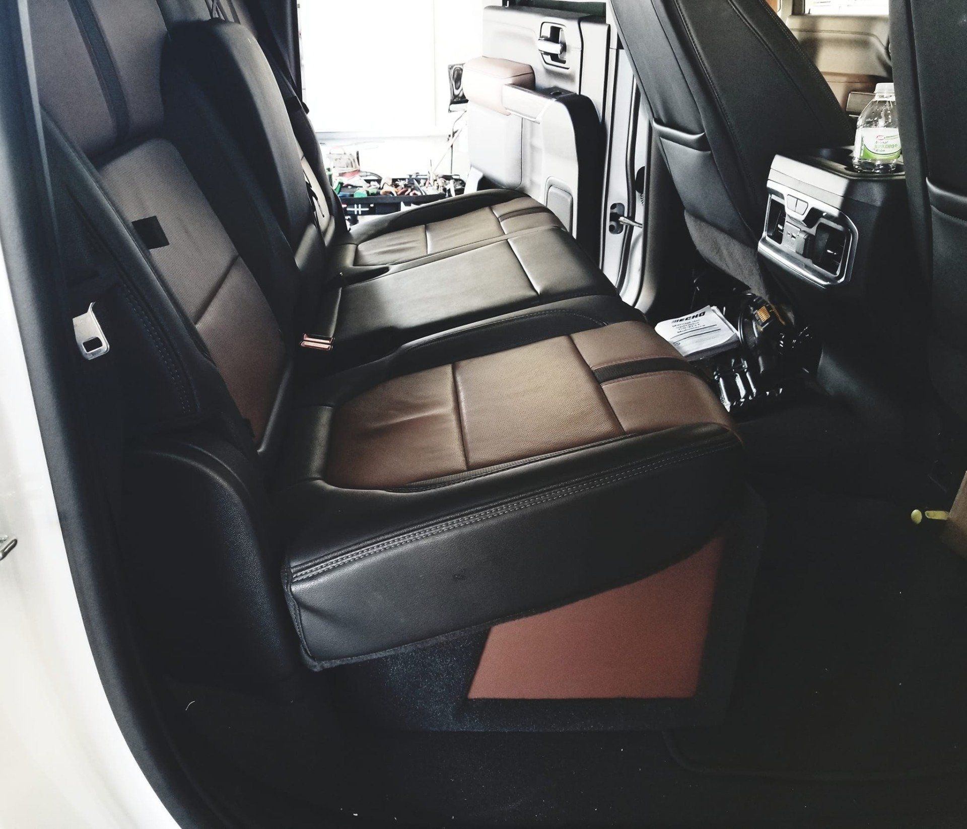 Brown and black leather truck backseat with console and water bottle.