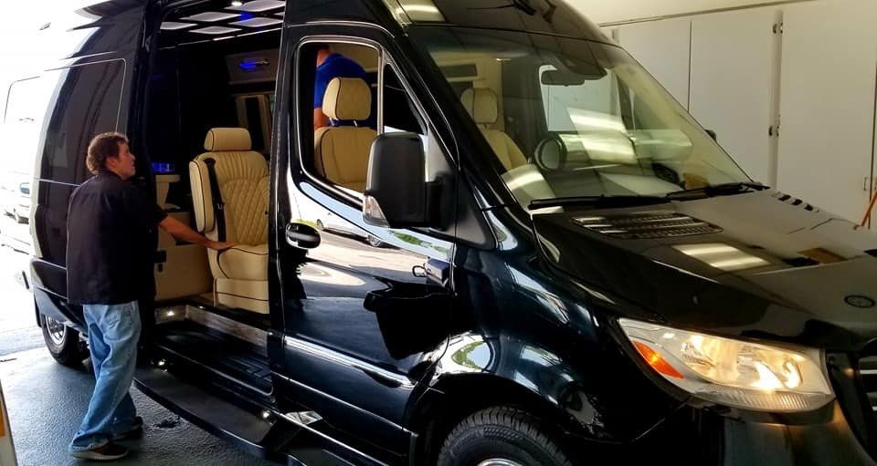 Black van with open side door. Man in blue shirt stands by the open door, looking inside.