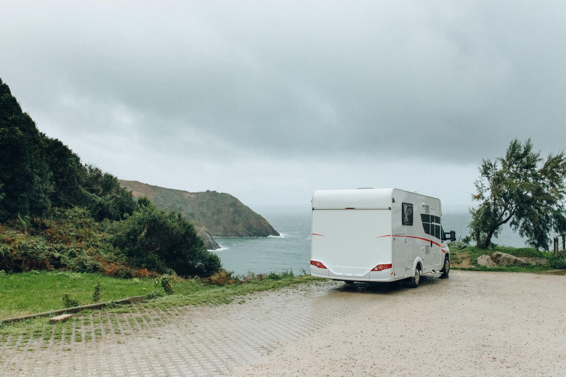 White campervan parked near coastline on a cloudy day.