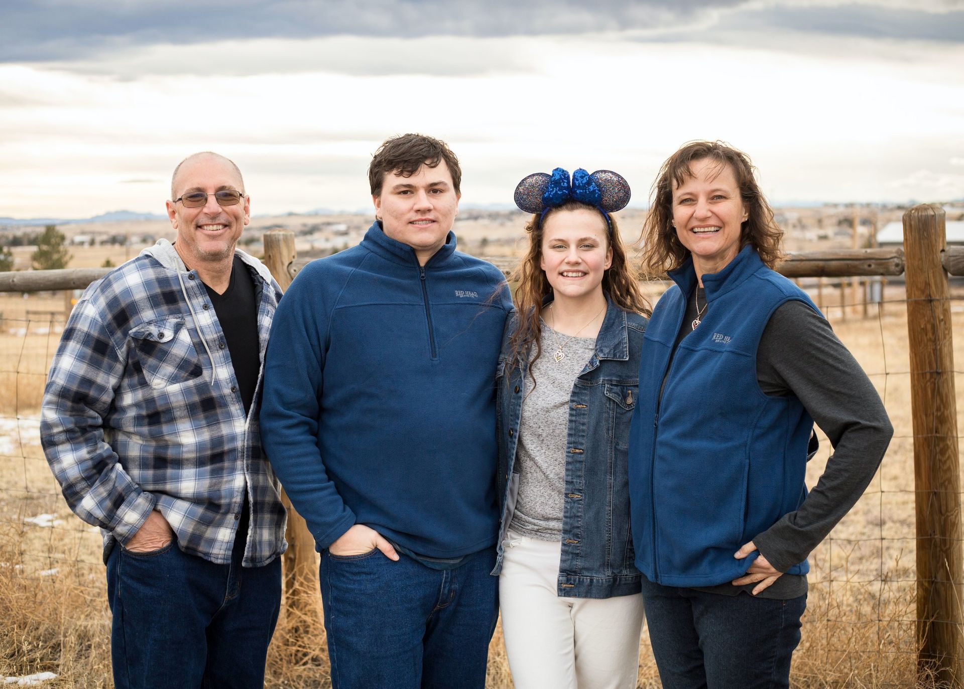 A family is posing for a picture in front of a fence in a field.