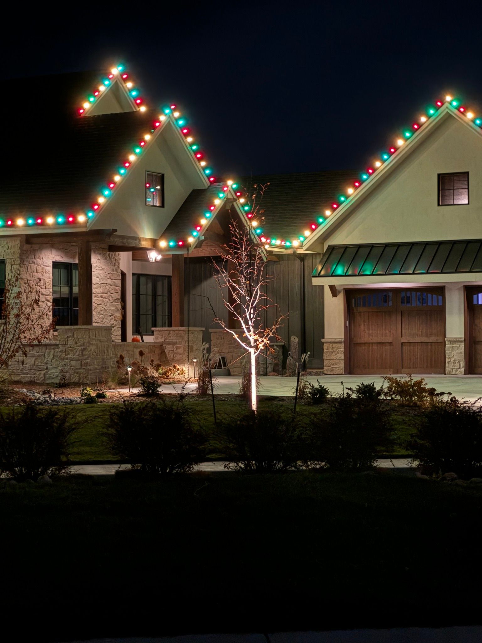 A house with christmas lights on the roof and a tree in front of it