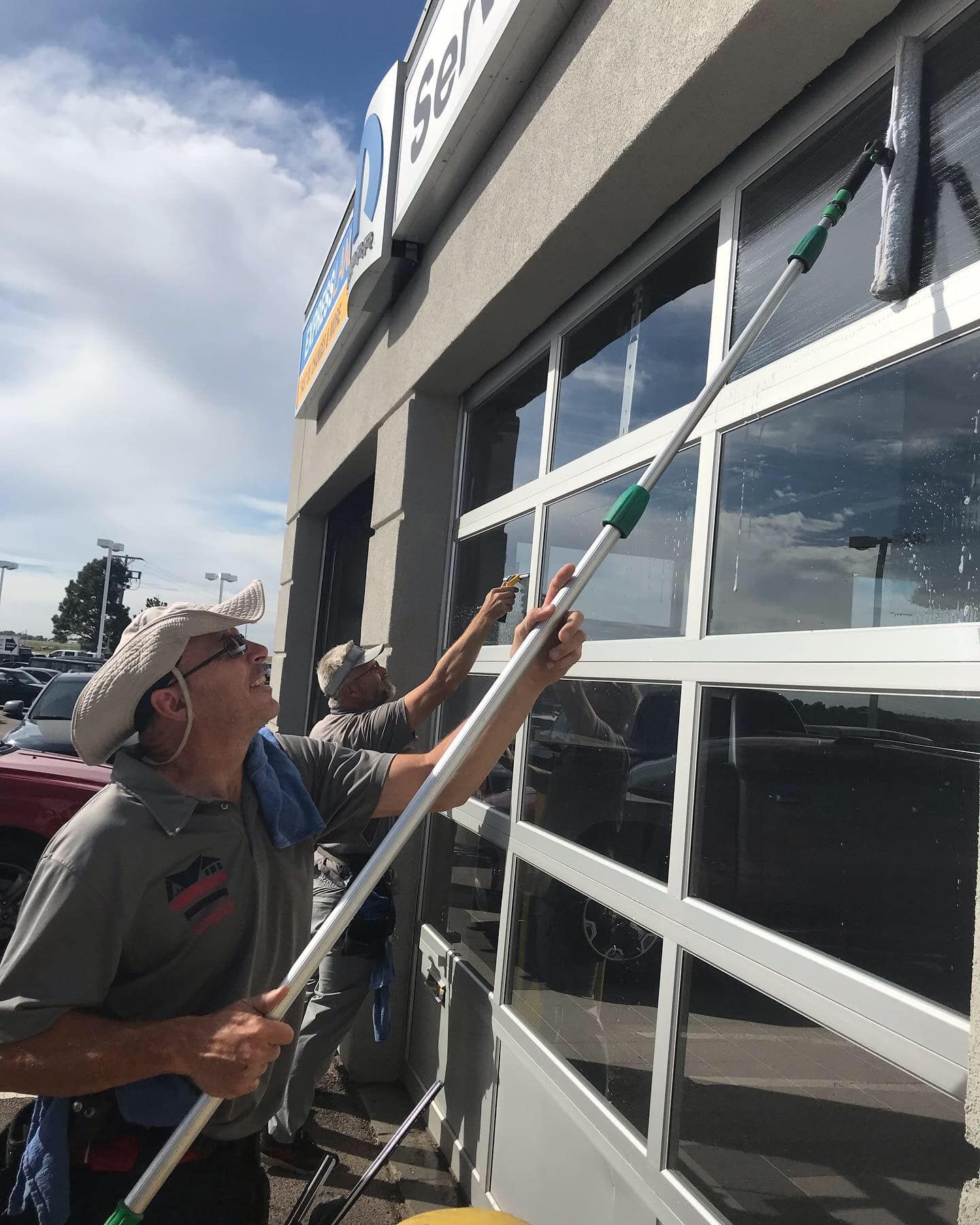 Two men are cleaning a garage door with a long pole.