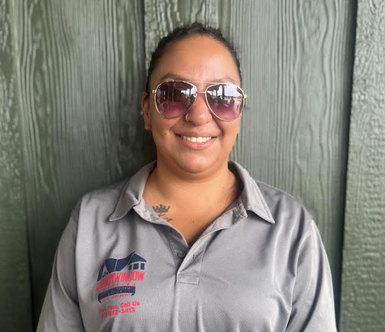 A woman wearing sunglasses and a gray shirt is smiling.