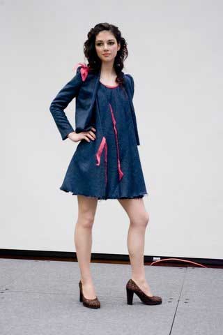 A woman in a blue dress and pink jacket is standing on a stage.