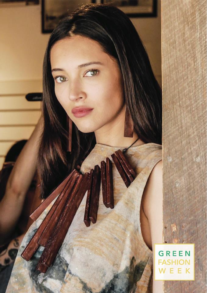 A woman wearing a necklace and earrings is standing next to a wall.