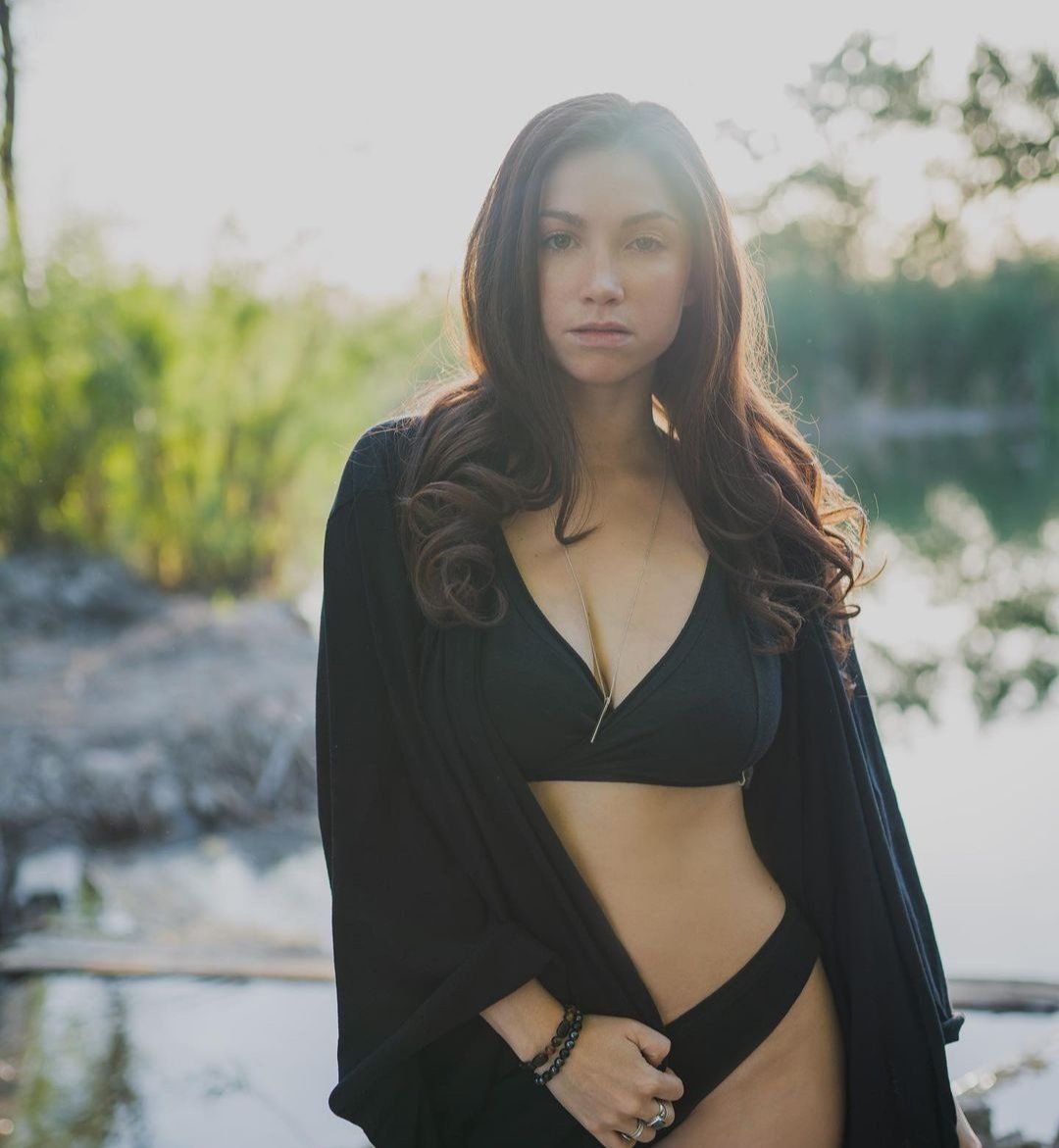 A woman in a black bikini is standing in front of a body of water