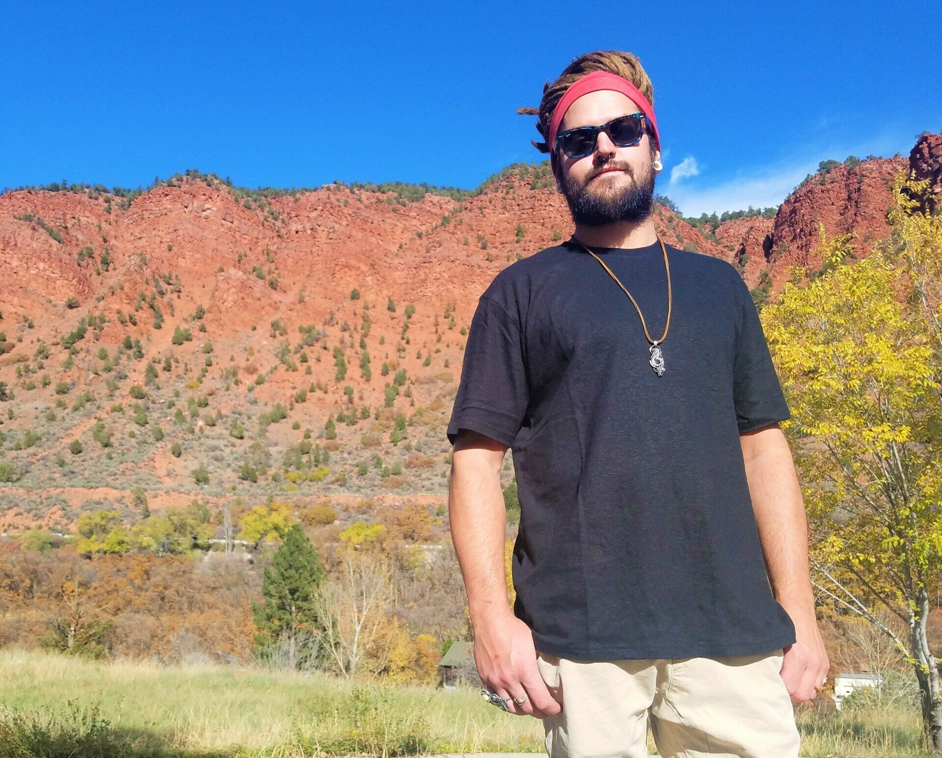 A man wearing sunglasses and a headband stands in front of a mountain