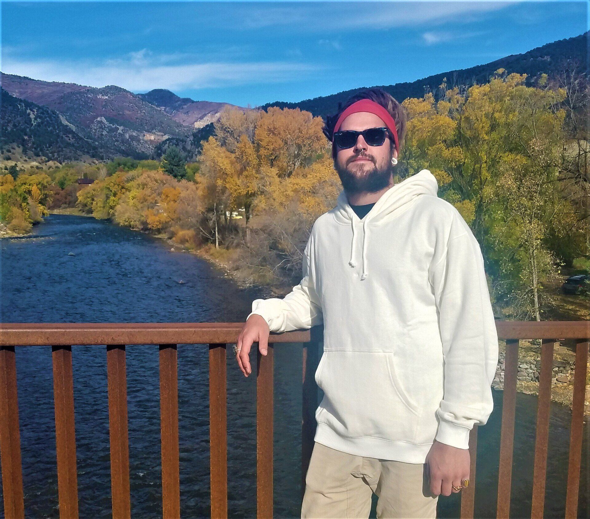 A man in a white hoodie stands on a bridge over a river