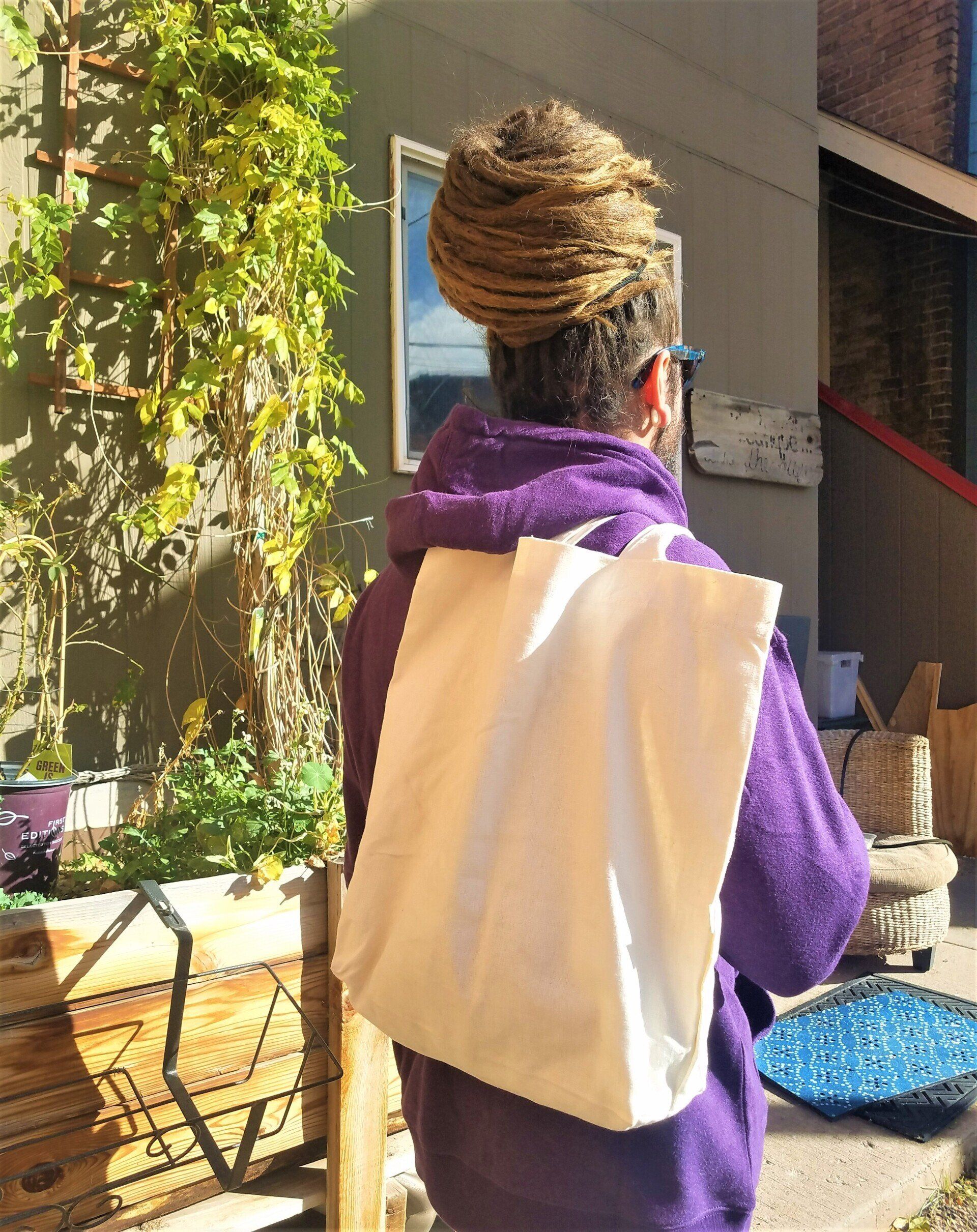 A woman in a purple hoodie is carrying a white tote bag.