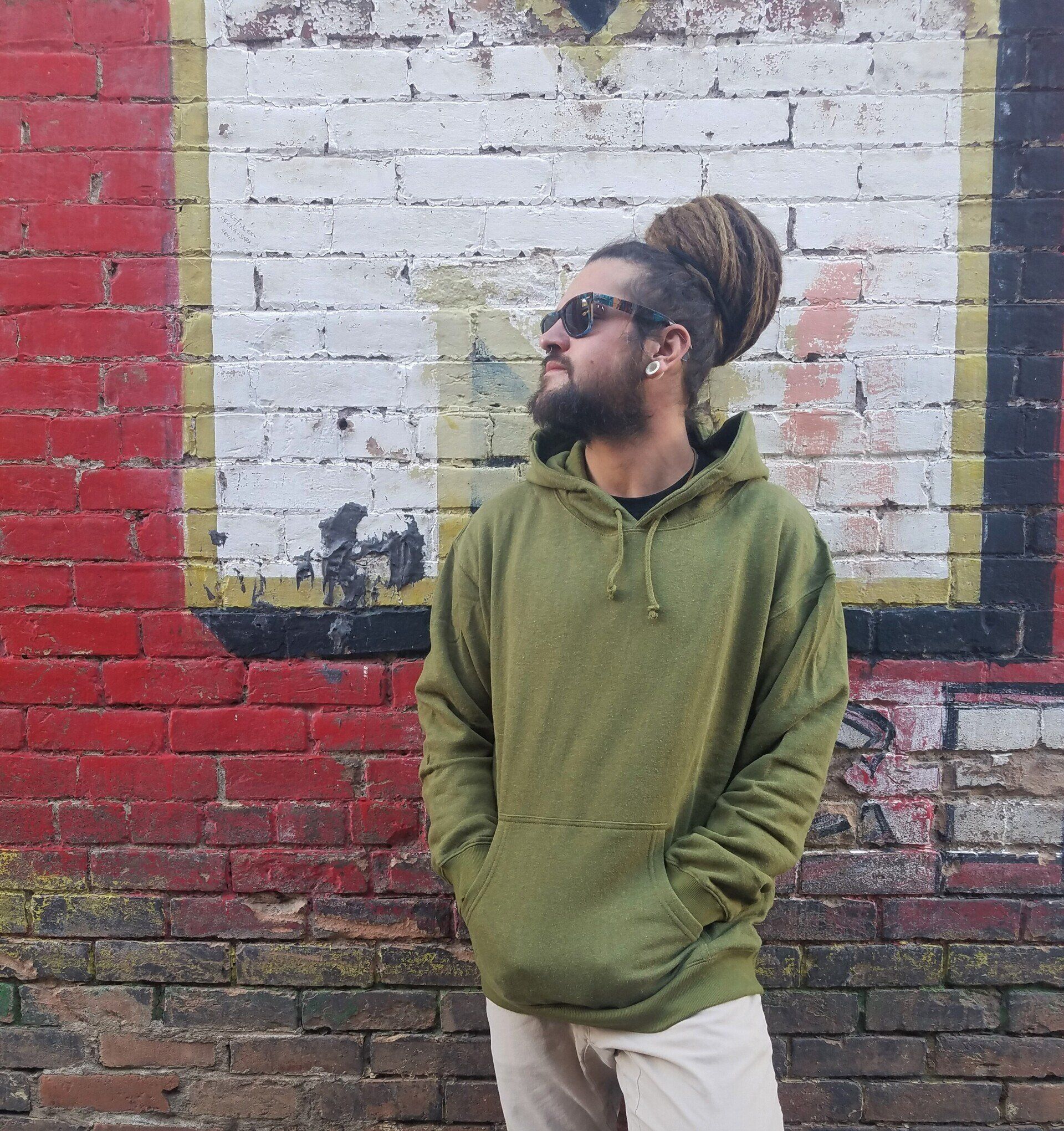 A man in a green hoodie is standing in front of a brick wall