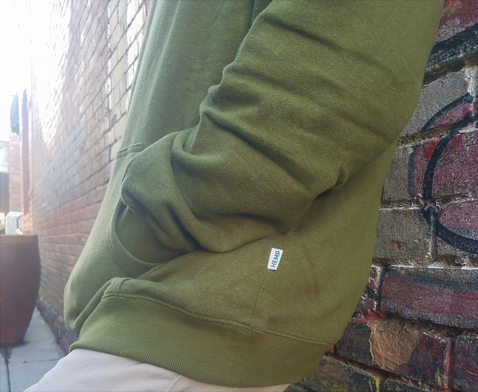 A person wearing a green hoodie is standing in front of a brick wall.