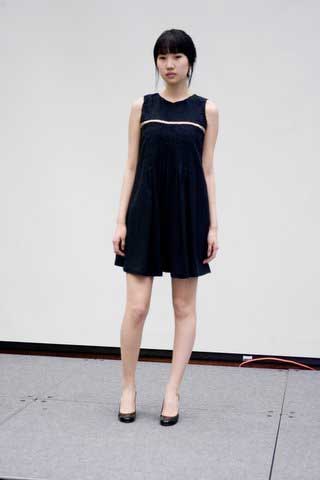 A woman in a black dress is standing in front of a white wall.