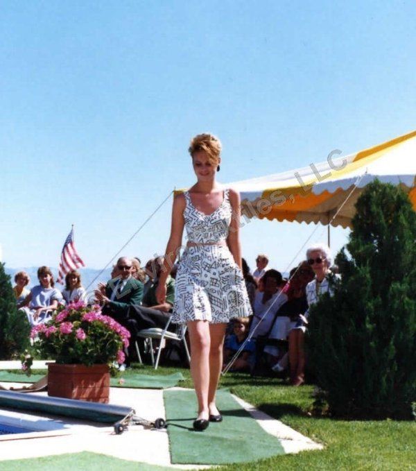 A woman in a dress walks down a runway in front of a tent that says llc