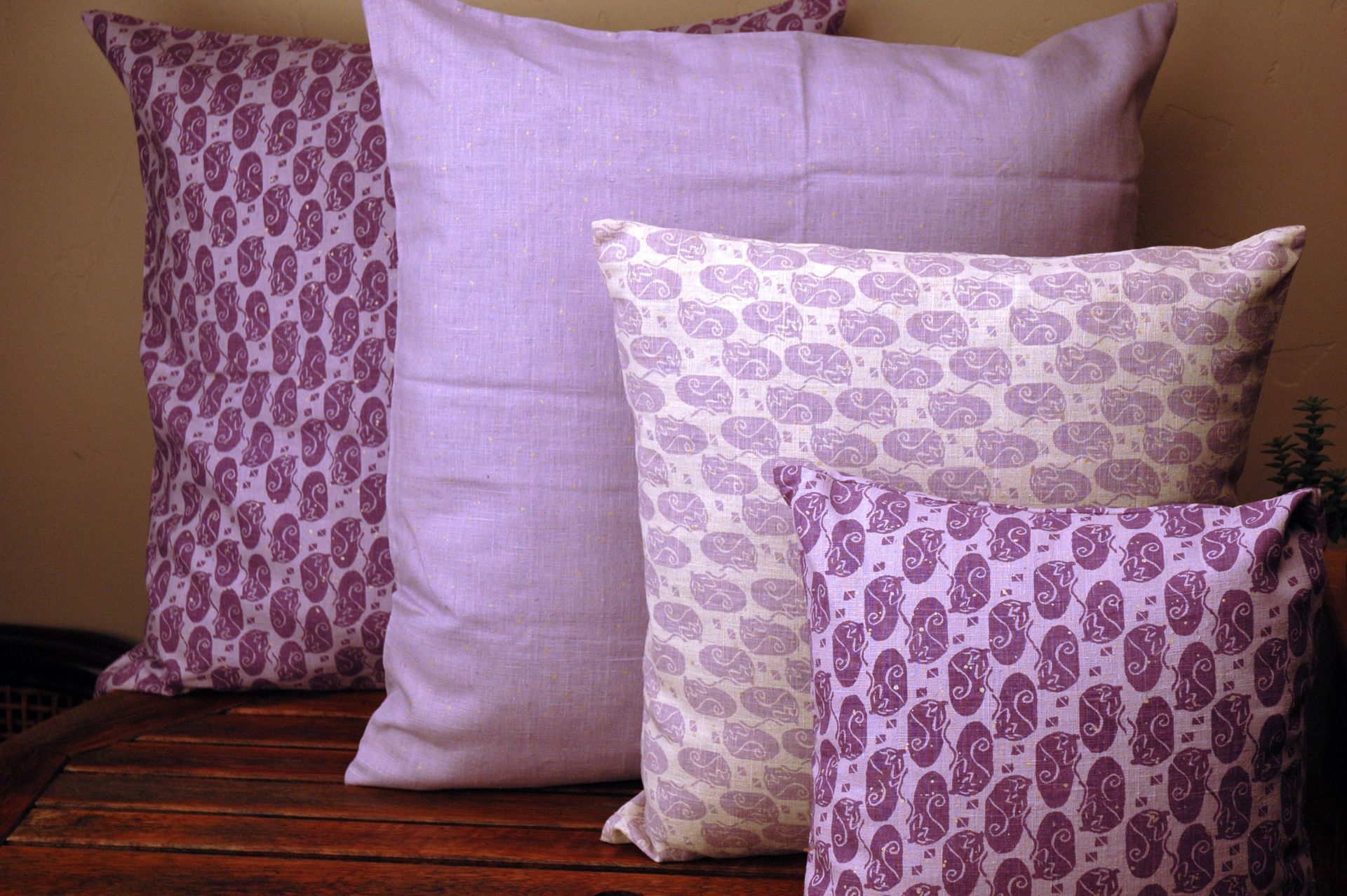 Three purple and white pillows are sitting on a wooden table