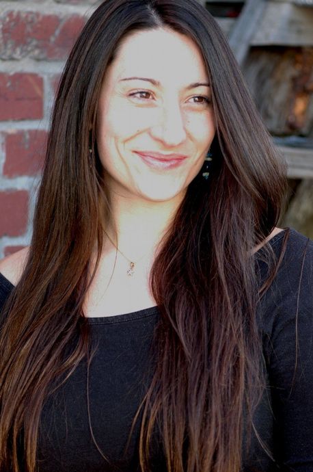 A woman with long hair is smiling in front of a brick wall.