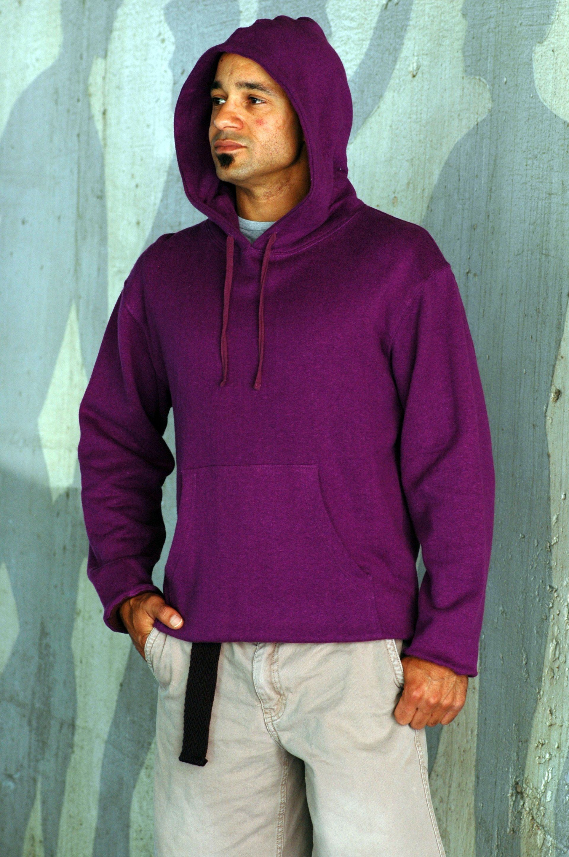 A man wearing a purple hoodie is standing in front of a wall