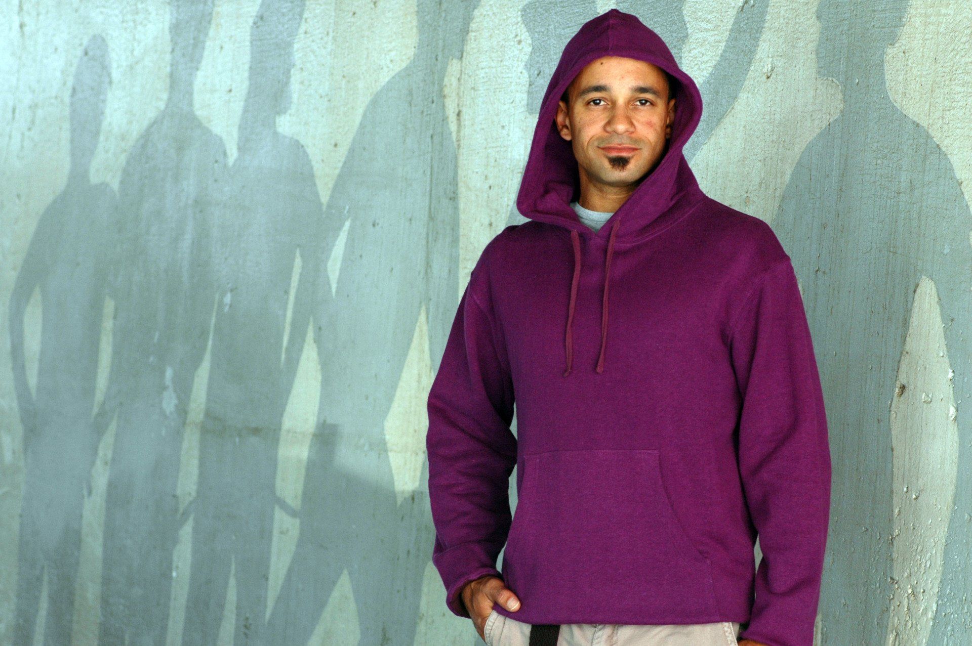 A man in a purple hoodie is standing in front of a wall