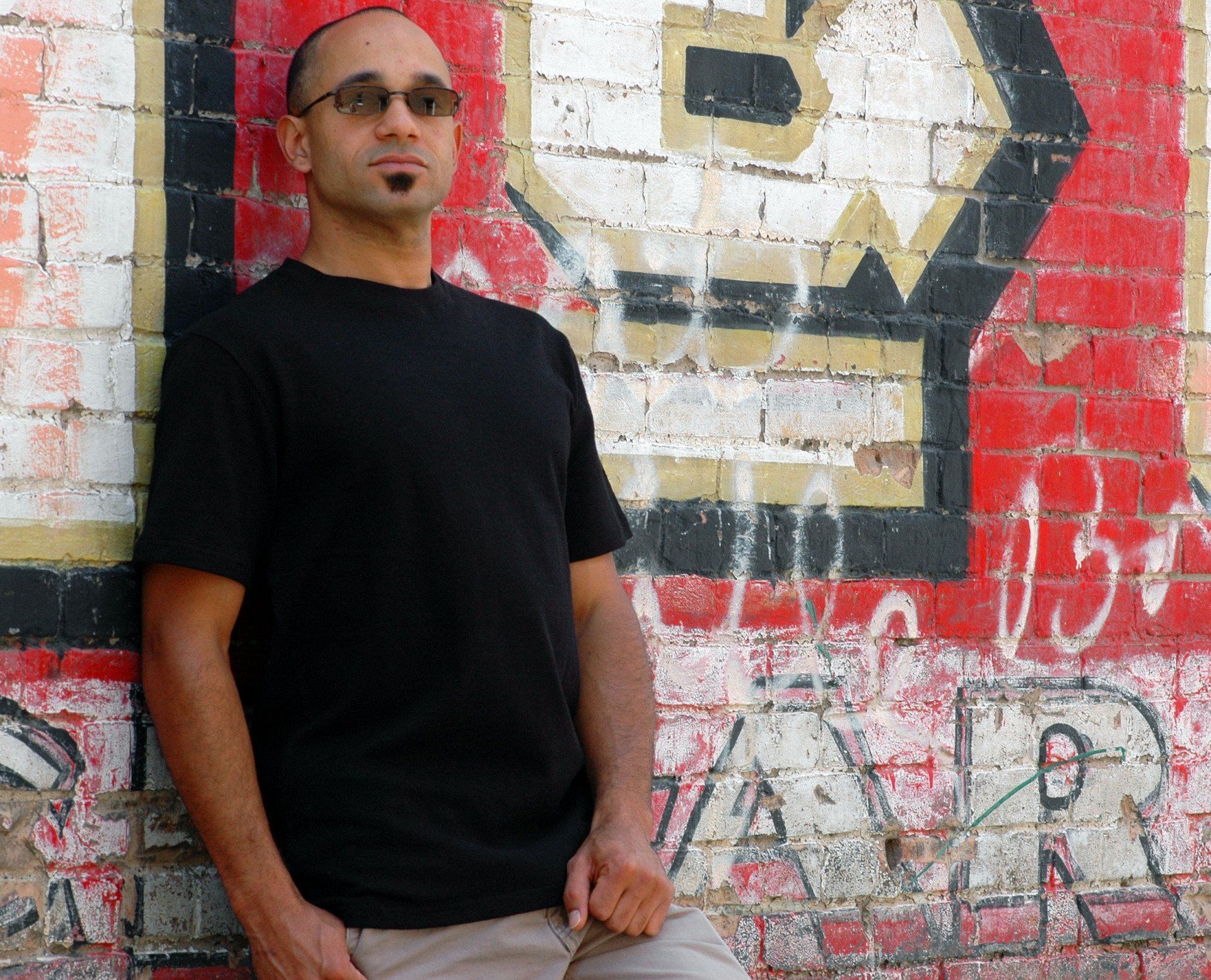 A man leaning against a brick wall with the letter b painted on it