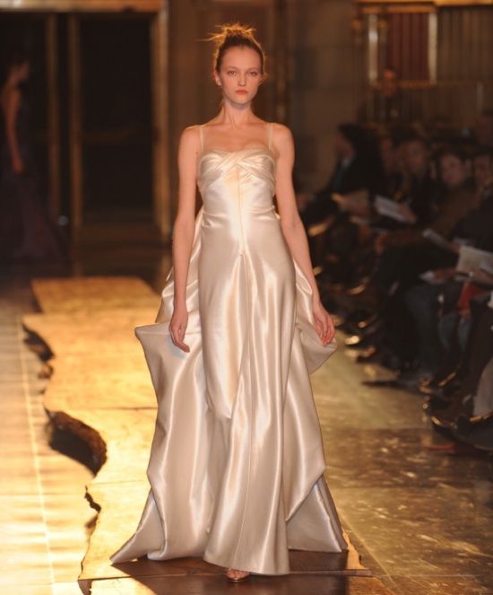 A woman in a white dress is walking down a runway