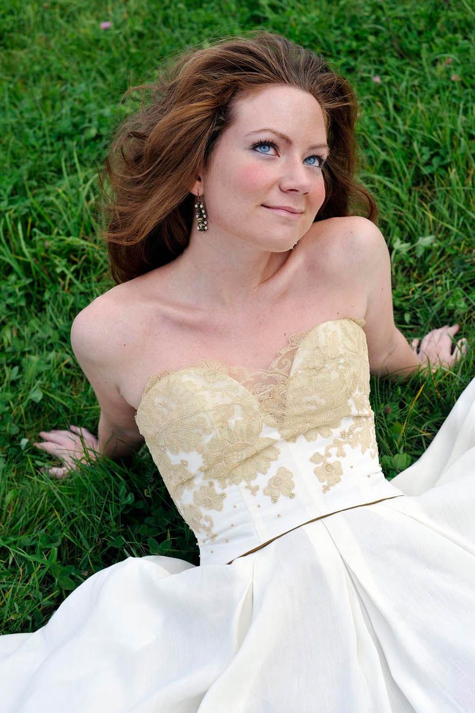 A woman in a white and gold wedding dress is laying in the grass.