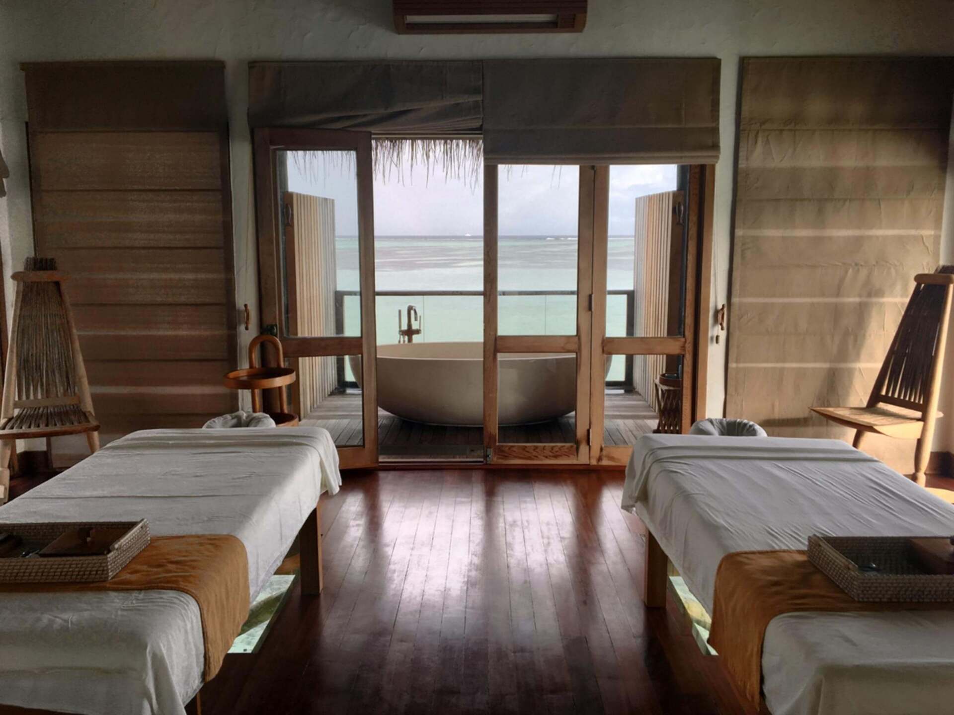 A room with two massage tables and a bathtub with a view of the ocean.