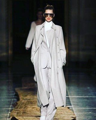 A woman is walking down a runway wearing a trench coat and sunglasses.