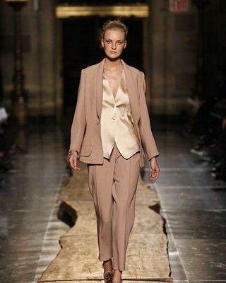 A model walks down a runway wearing a tan suit