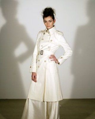 A woman in a white trench coat is standing in front of a white wall