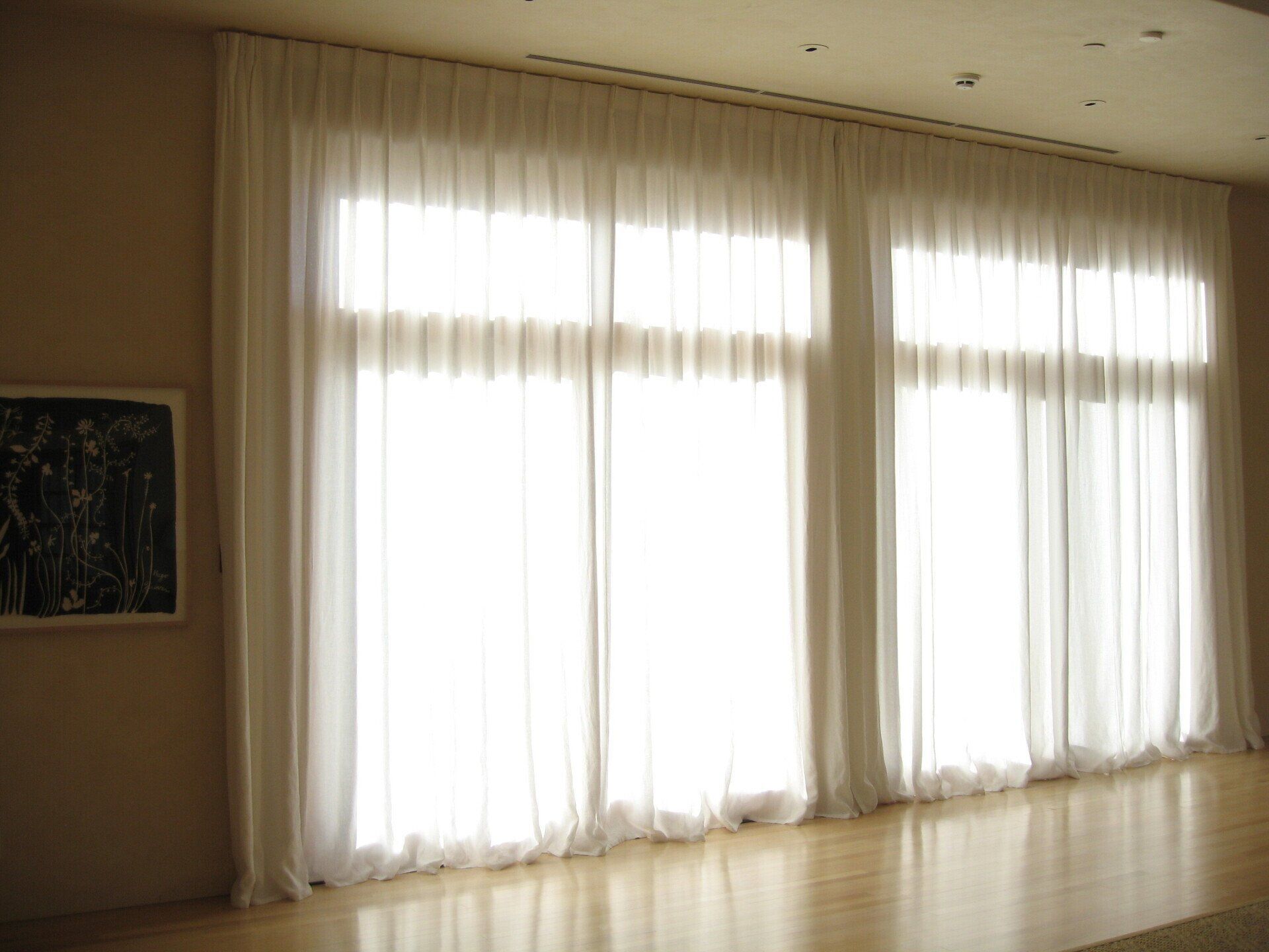 A living room with a lot of windows and white curtains.