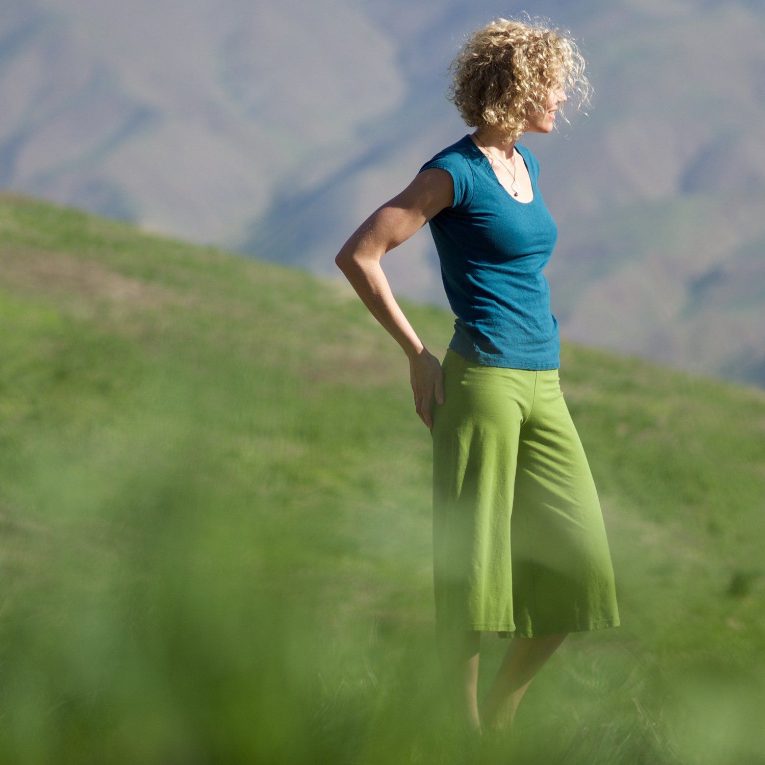 A woman in a blue shirt and green pants is standing in a grassy field