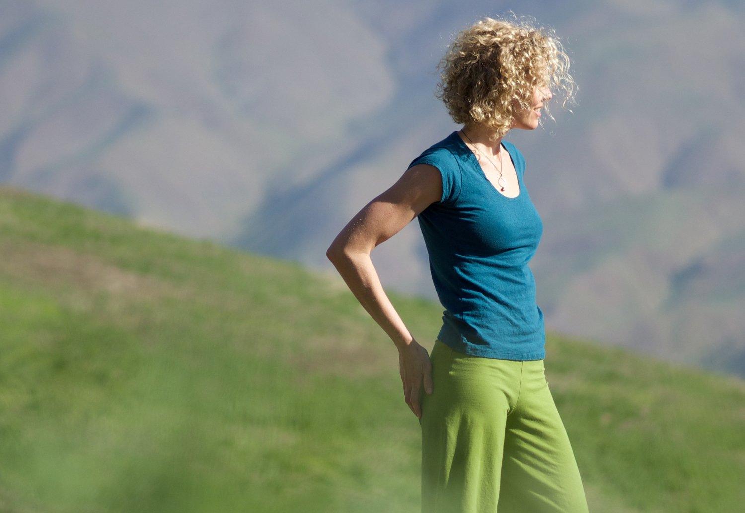 A woman in a blue shirt and green pants is standing on top of a grassy hill.