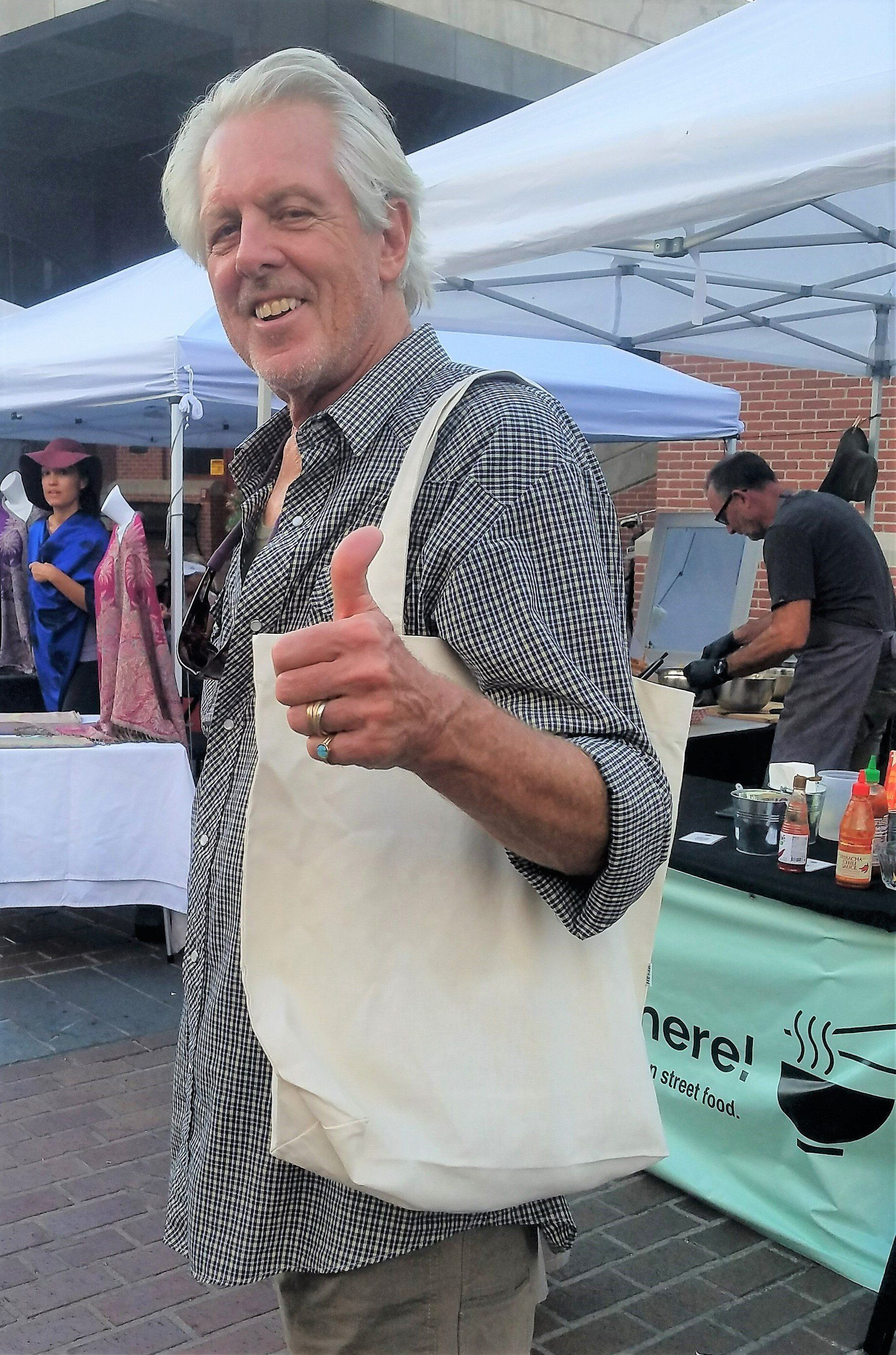 A man is giving a thumbs up while holding a tote bag.