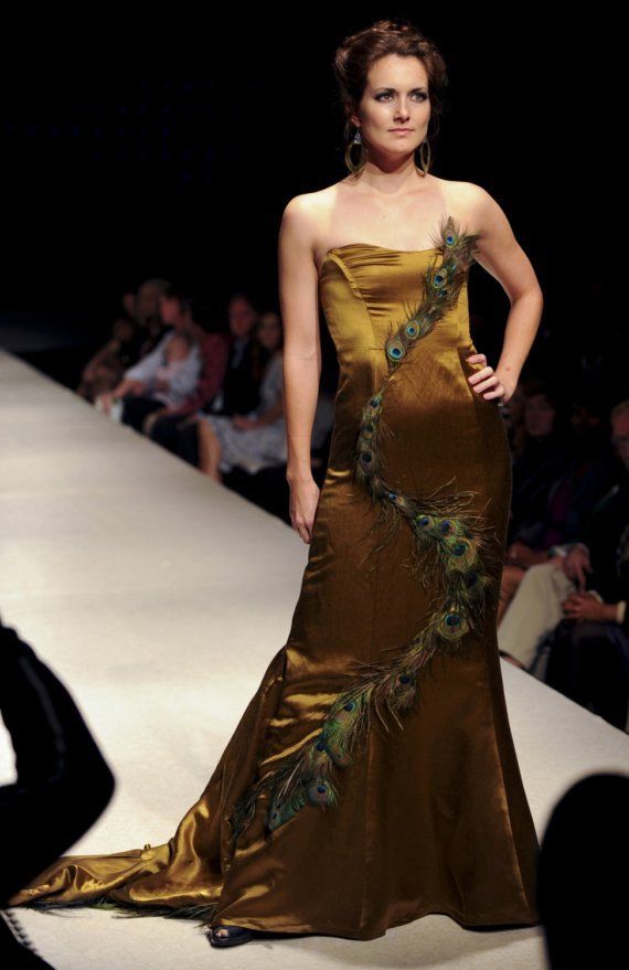 A woman is walking down a runway wearing a peacock dress