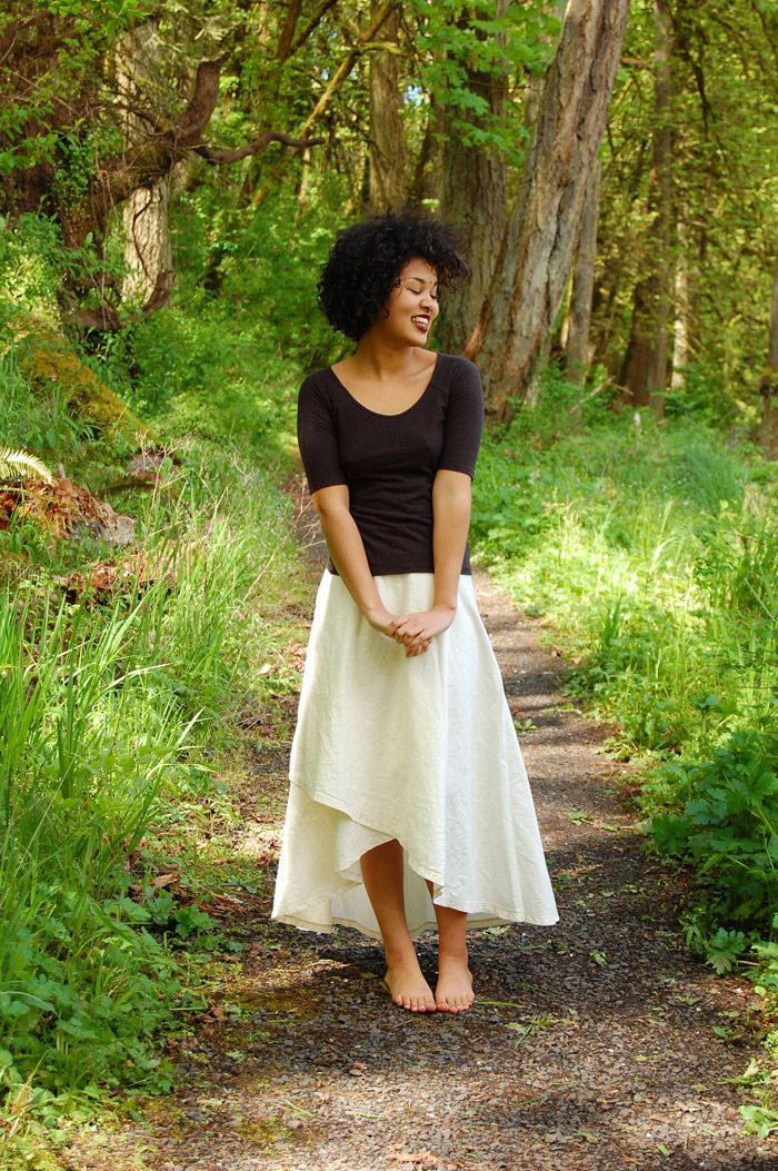 A woman in a white skirt is standing on a path in the woods.