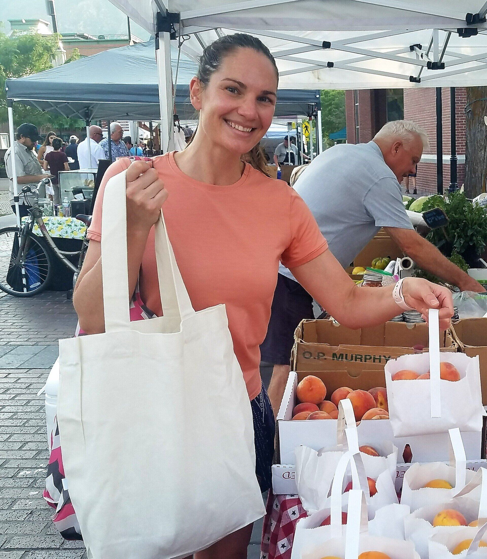 A woman is holding a white tote bag at a farmers market