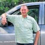 A man in a green striped shirt is standing next to a truck.