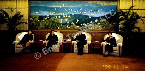 A group of people sitting in chairs in front of a large painting dated 1999