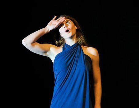 A woman in a blue dress is covering her face with her hand.