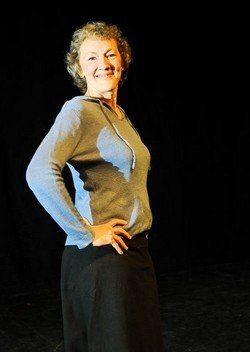 A woman in a blue sweater and black skirt is standing with her hands on her hips