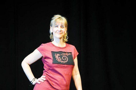 A woman in a red t-shirt is standing in front of a black curtain.