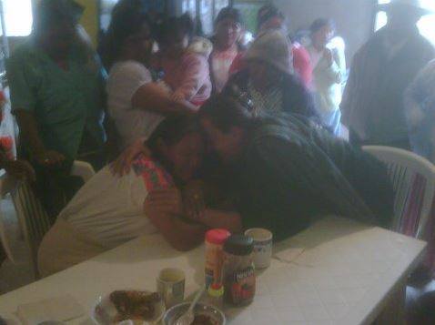 A group of people are standing around a table with a man laying on it.