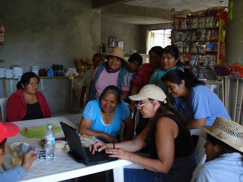 A group of people are sitting around a table looking at a laptop.