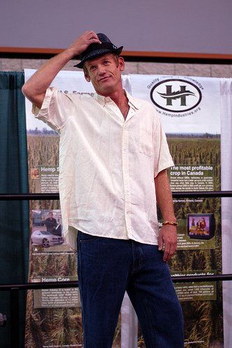 A man wearing a hat and a white shirt is standing in front of a poster with the letter h on it.