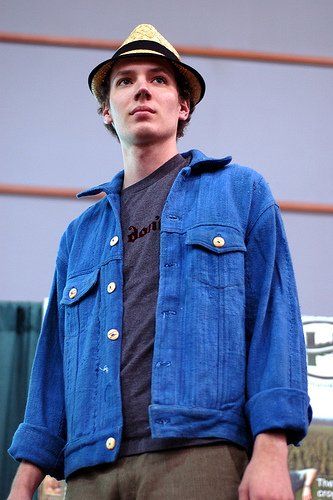 A young man wearing a hat and a blue denim jacket.