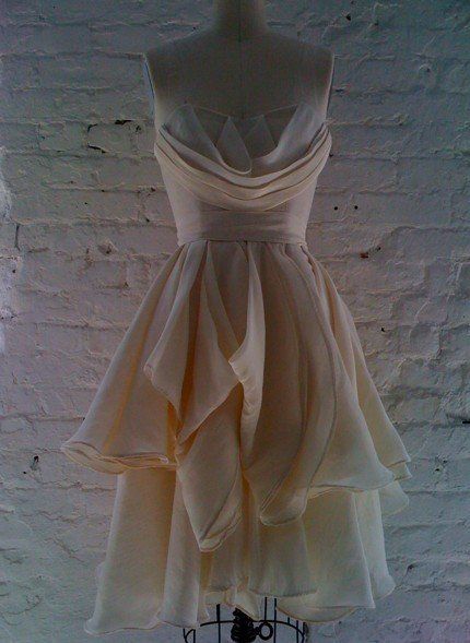 A white dress is on a mannequin in front of a white brick wall.