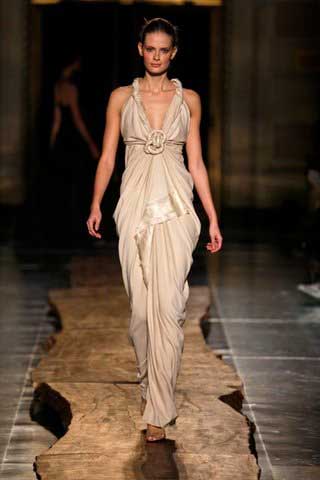 A woman in a long white dress is walking down a runway.