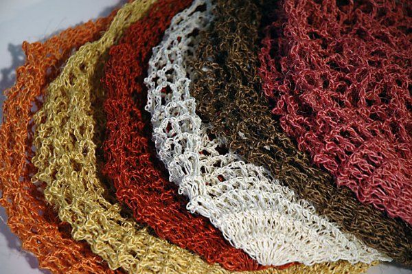 A bunch of different colored crocheted scarves are stacked on top of each other on a table.