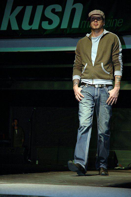 A man is walking down a runway in front of a kush magazine sign