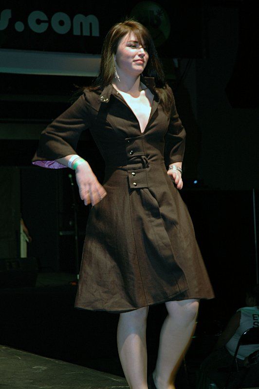 A woman in a brown dress is standing in front of a sign that says j.com